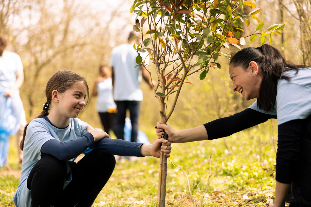 Mother and child planting trees with a group, sponsored by TreeTherium’s green initiatives and project sponsors.